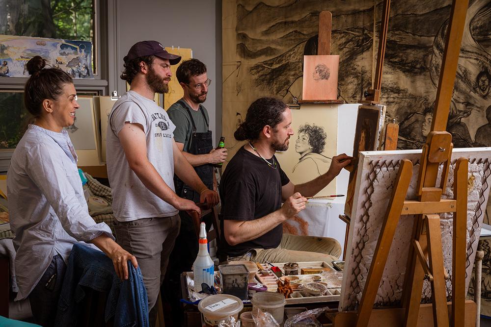 Jill Hooper, Anselme Long and Caleb Clark look on as Christopher Holt works on canvas.