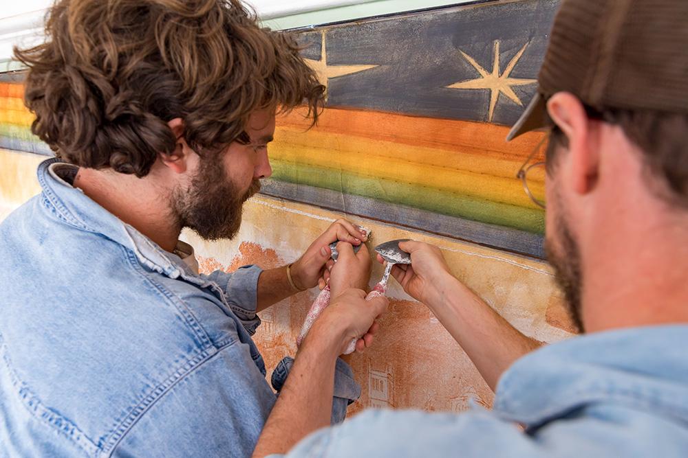 Anselme Long and Caleb Clark paint a rainbow, which arches over the center of the fresco.