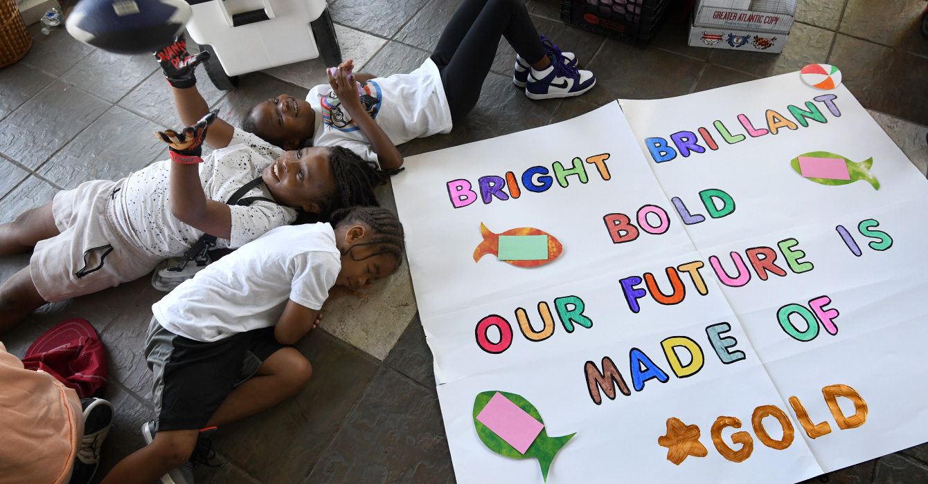 Three summer campers lying next to a colorful sign