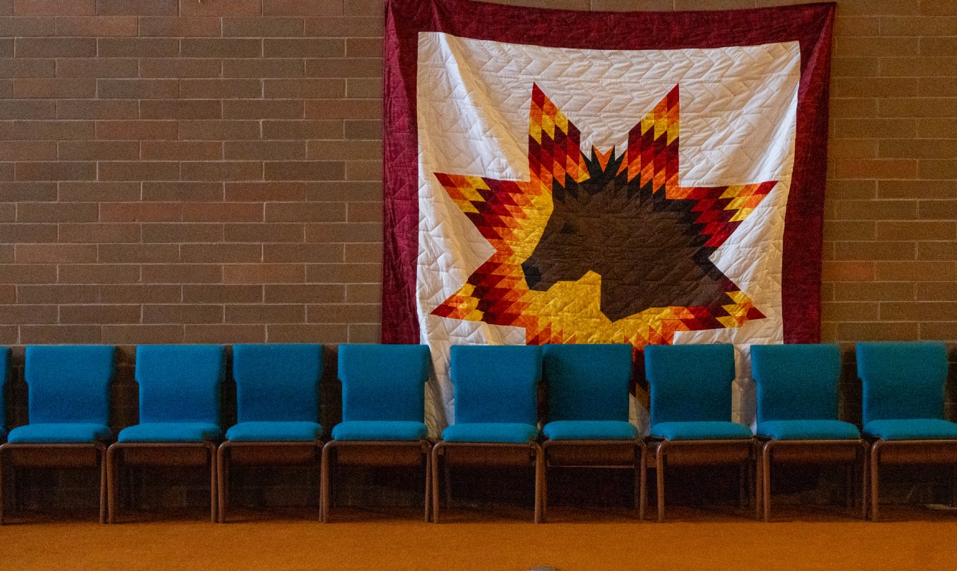 Image of a quilt of a horse hung on a brick wall behind a group of chairs