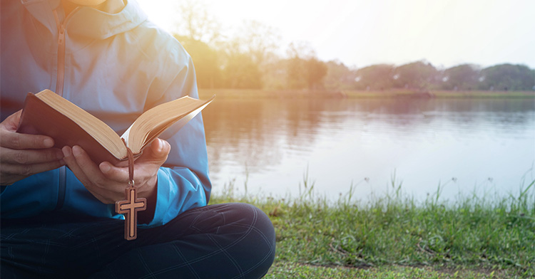 Person with a Bible sitting by a quiet pond