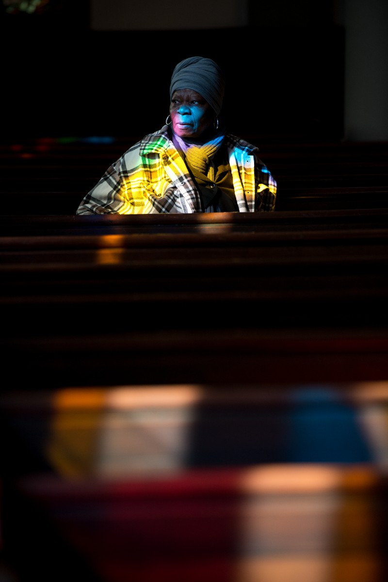 photo of a woman sitting in a pew with light from stained glass shining on her