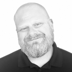 A black and white photo of a bald man with a beard smiling.