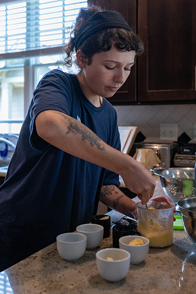 A young woman wearing a dark blue shirt and headband scoops butter out of a food processor.