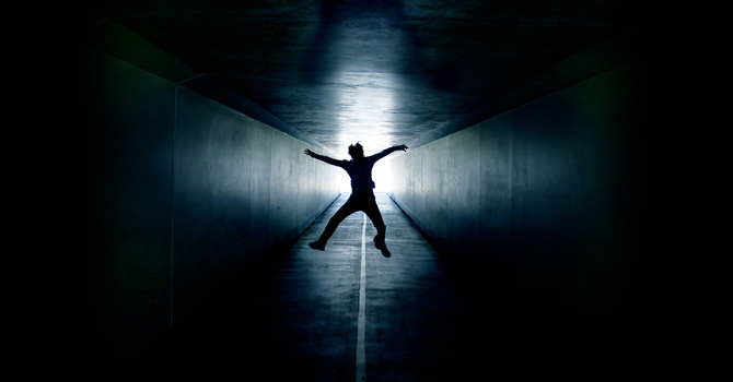 Man jumping for joy in a tunnel; light forms a cross shape behind him
