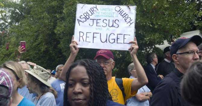 Protest sign reads "Asbury United Methodist Church, Charlottesville, VA" and "Jesus was a refugee"