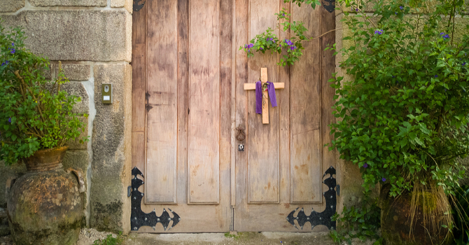 Simple wooden cross draped with purple cloth hangs on a church door