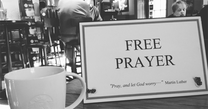 A sign saying "FREE PRAYER" and "'Pray, and let God worry - Martin Luther'" on a table in a coffee shop