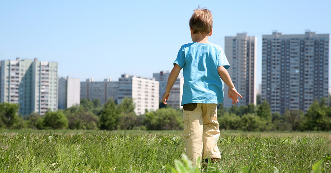 Small boy walking alone in a field, city skyline in the distance