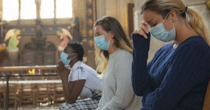 3 young women in face masks praying in a church